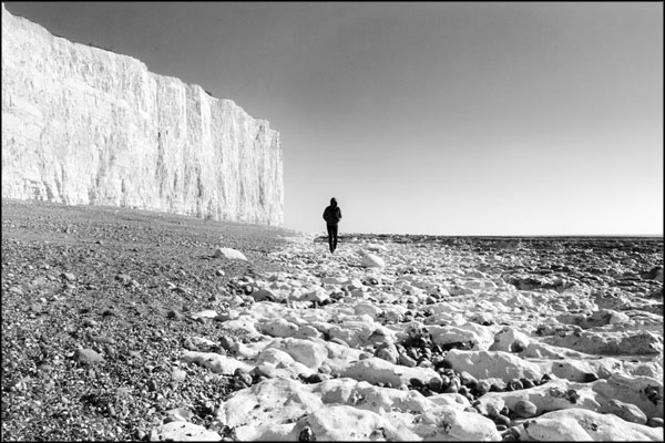 A-033. Man strolling along the foot of the Seven Sisters - by Greig Clifford